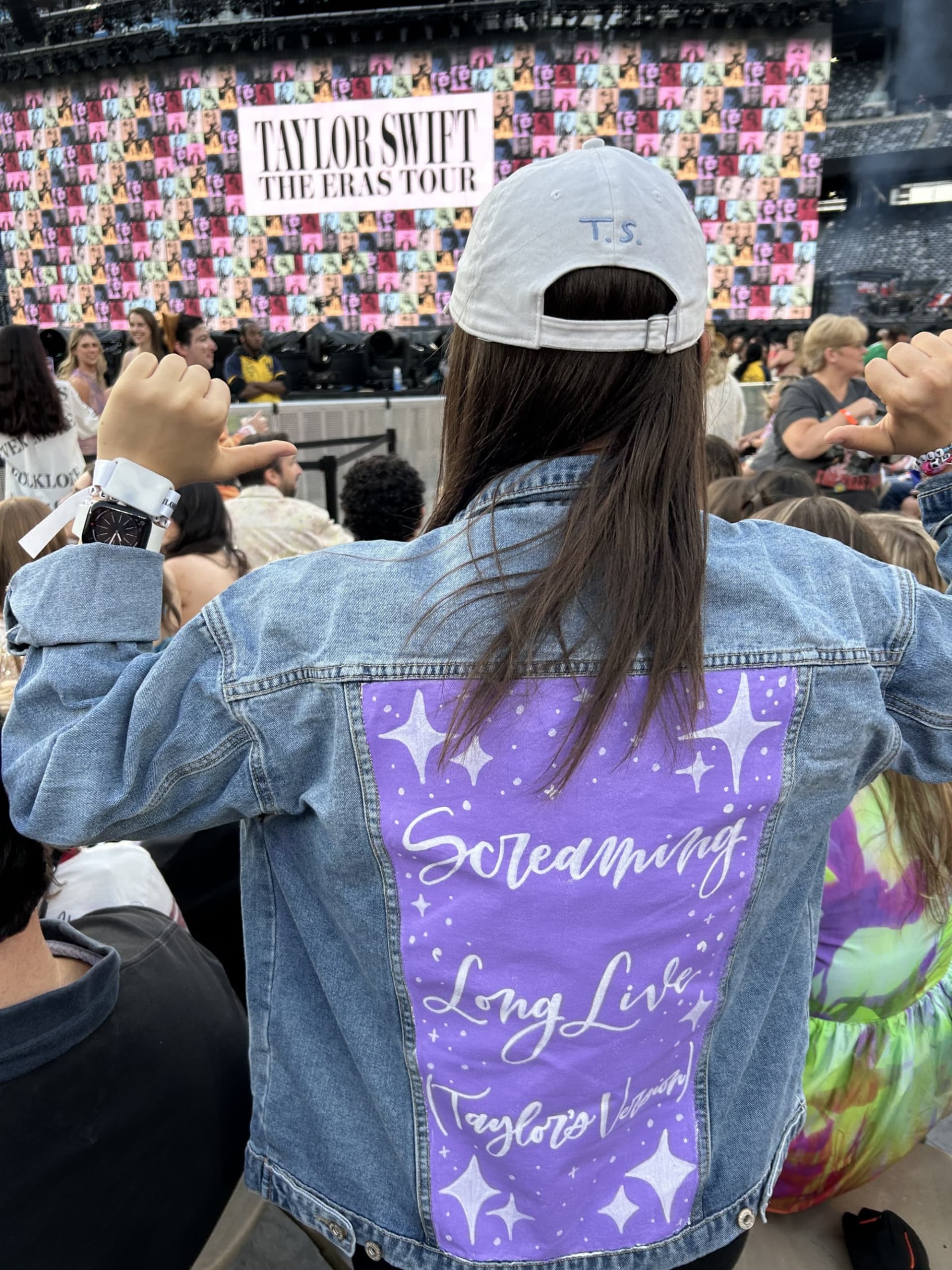 A picure showing the back of Ava Jeffs as she points to her painted jacket at the Taylor Swift concert.