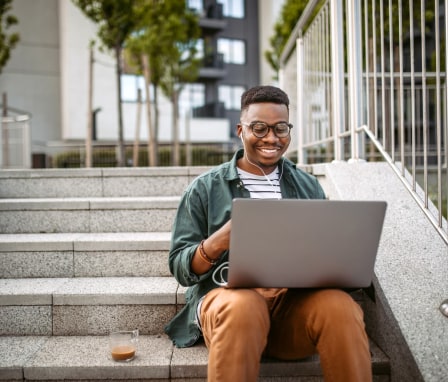 Young man smiling while using laptop, sitting on outside stairs