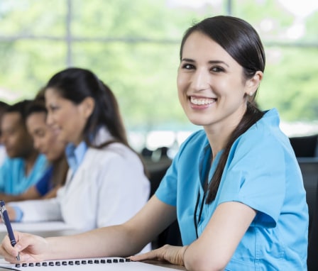 Confident nursing student smiles while taking notes in classroom.