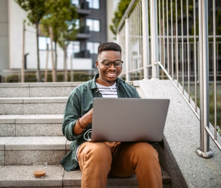 Young man smiling while using laptop, sitting on outside stairs