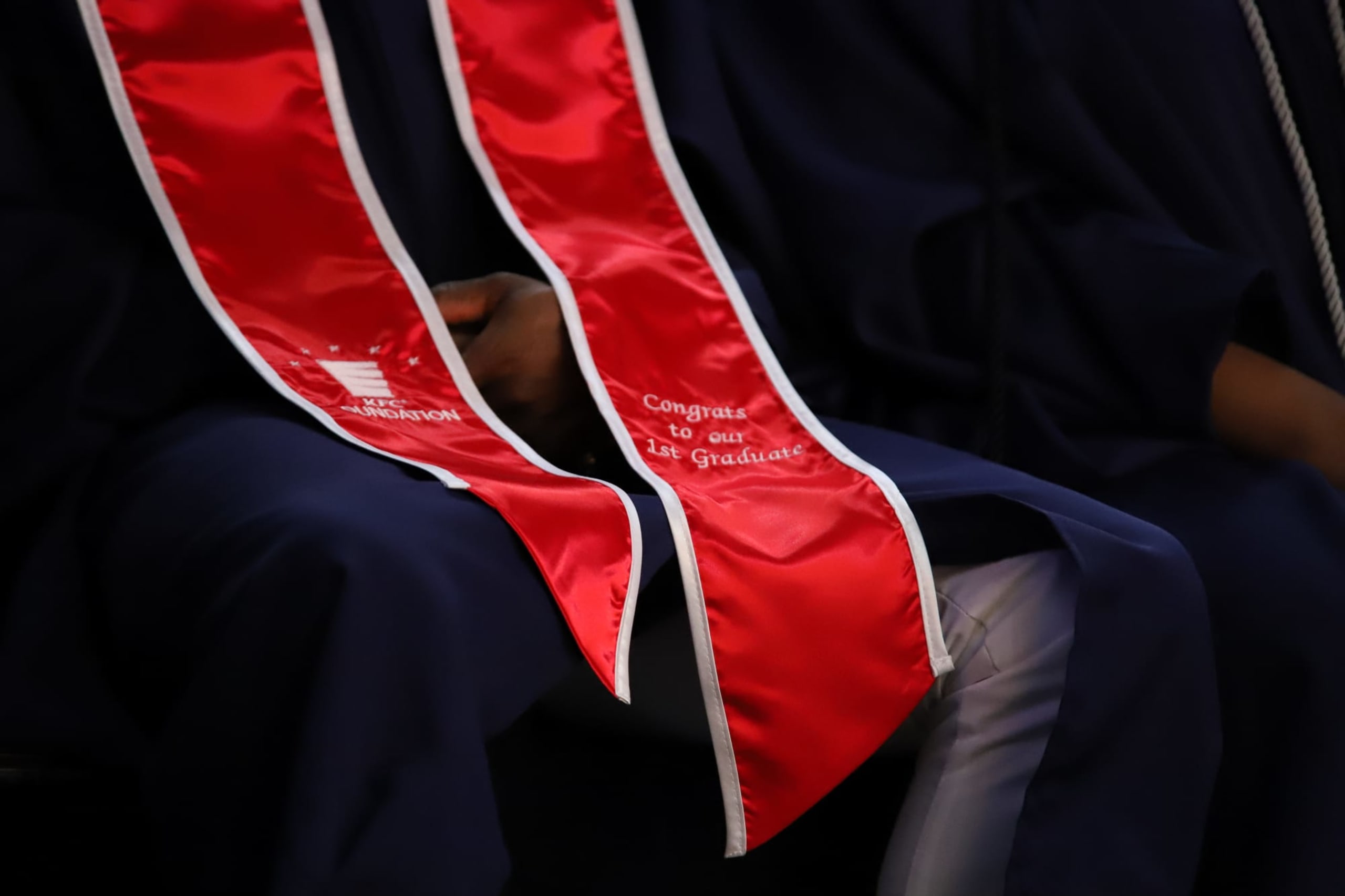 Close-up of Kevon's red graduation sash, reading: KFC Foundation, Congrats to our 1st graduate.