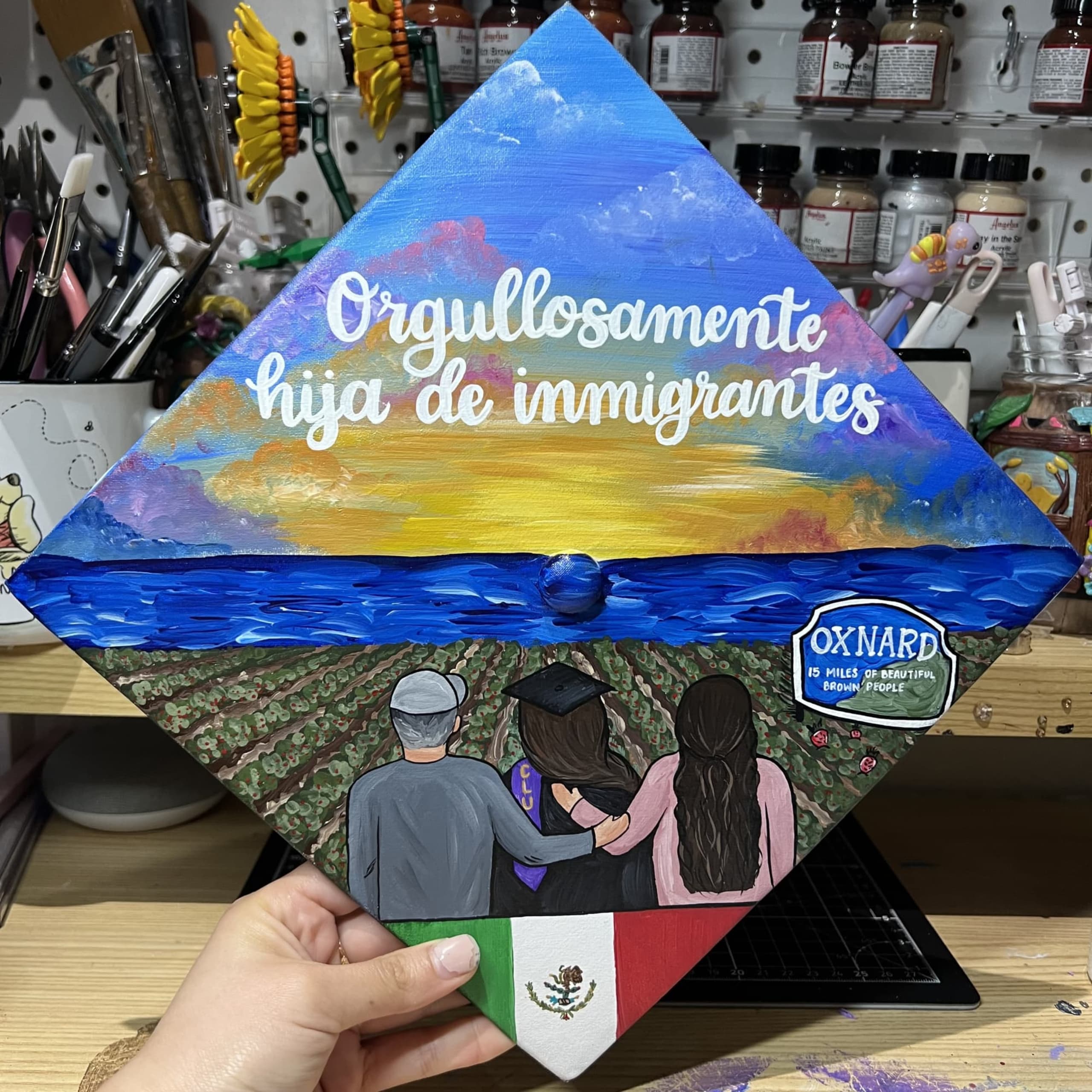 A graduation cap painted with the graduate and her parents looking into a sunset.