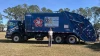 A young woman stands in front of a blue recycle truck with her artwork displayed on the side: "Reuse to Use"