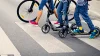 Kids walking scooters and a bike across the street - you can only see feet and wheels