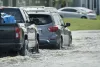 Flooded road with evacuating cars and surrounded with water houses in suburban residential area.