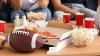 A football on a table with pizza, popcorn and red cups, surrounded by people