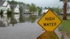 A high water sign sits in flood waters in a residential neighborhood