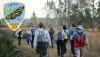 Hikers on a trail surrounded by trees and plants. Upper left corner is the 2024-2025 Hiking Spree  badge that features a Zebra Longwing black and yellow butterfly on a leaf