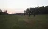 A large field with people hiking towards the trees and sunset