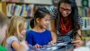 An adult showing a book to some kids in the library