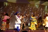 A group of Black dancer in bright costumes with the drummers in the background