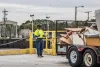 A man in a safety-yellow shirt directs a truck to back-up to the trash drop-off point