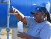A woman stands next to a water tank taking a collection into a bottle