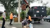 A crew helps load large items into a garbage truck with the help of a crane arm