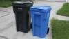 A green trash cart and a blue recycling cart sitting at the curb