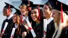 High School students in their cap and gowns holding rolled up "diplomas"