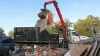 A man controls the scoop on the truck to put trash in the garbage ontainer