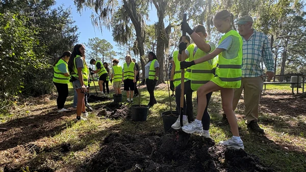 Students dressed in safety vests and gloves use shovels to dig holes at Lake Park to plant a total of 14 trees.