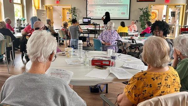 Seniors sitting at tables with handouts watching the instructor at the front of the room