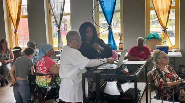 The instructor and a student working on a laptop and the instructor has a microphone in her hand to explain what's happening to the other students