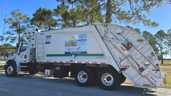 A white recycling hauler truck displays the winning artwork "Clean the Beach" - Protect wildlife by properly picking up trash and recyclables at the beach.