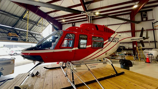 Red and white helicopter sits on a movable base inside a hangar