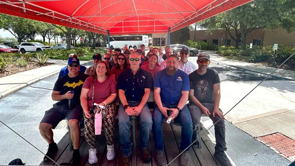 A group of veterans and their spouses sit in an open-air tour bus that is covered by a red canopy