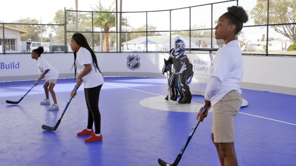 Kids in a street hockey rink holding hockey sticks with a goalie in the background