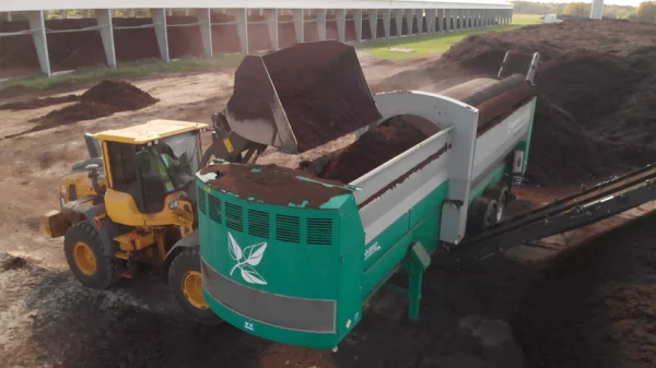 A front-end loader drops mulched yard cuttings and biosolids into the transport vehicle