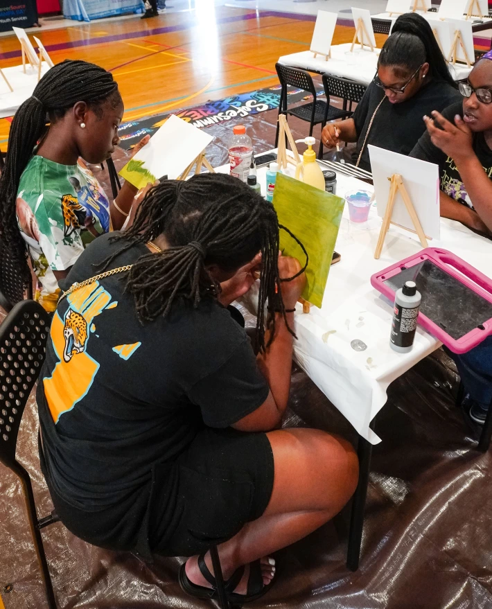 Four Black teens sit at a table painting