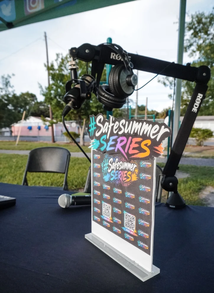 A #Safesummer Series sign sits on a table with podcast gear (headphones and microphones)