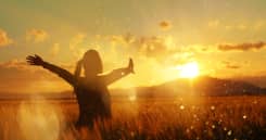 silhouette in the sunset, young woman with her arms raised enjoying summer twilight in the middle of nature.