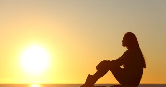 Woman silhouette watching sun in a sunset