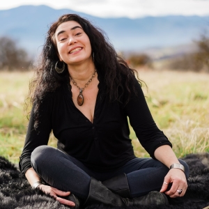 Veege Ruediger sitting cross legged in a field with mountains in background