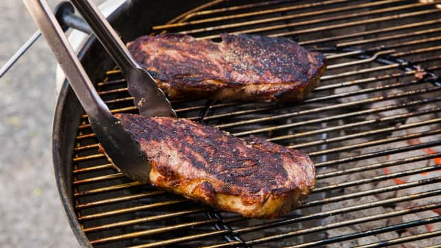 grilling steaks over charcoal grill