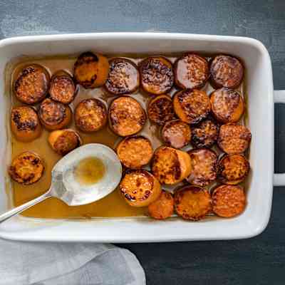 Candied sweet potatoes in a baking dish with a serving spoon