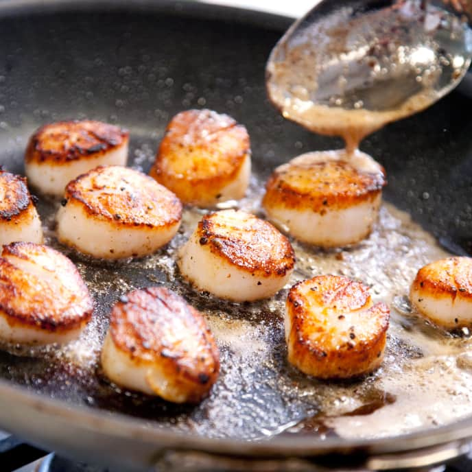 Woman measuring the temperature of a scallop in a frying pan with