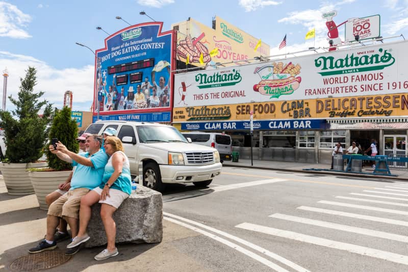 A group takes a selfie across the street from Nathan's Famous Hot Dogs on Coney Island, New York City.