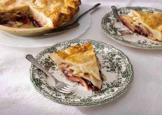 Slice of pie on a plate with a fork, whole pie in background