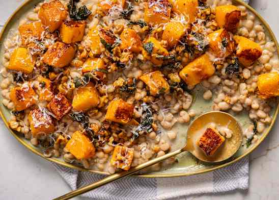 Cacio e Pepe Beans with Squash, Sage, and Walnuts on an oval-shaped serving dish with a round golden spoon