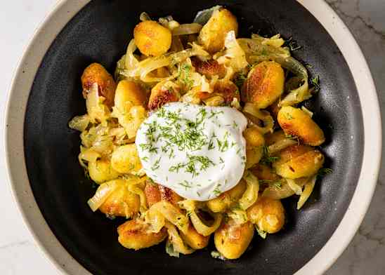 Crispy Pan-Fried Gnocchi with Buttery Onions and Sauerkraut sprinkled with dill and topped with a dollop of sour cream