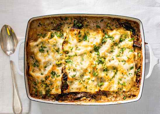 Mushroom lasagna in a white baking pan with serving spoon