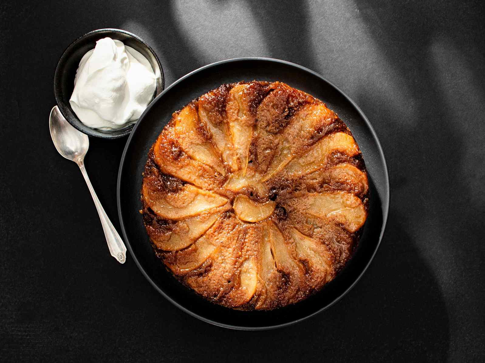 Pear-Walnut Upside-Down Cake on a serving plate, with bowl of whipped cream on the side