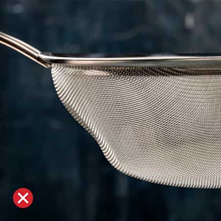 A fine-mesh strainer with a deformed, lumpy-looking basket and a red x in the bottom left corner.