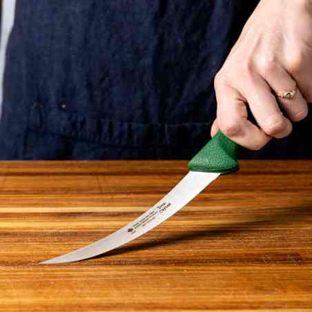 A boning knife with a green handle is pressed against a cutting board, showing a distinct flex.