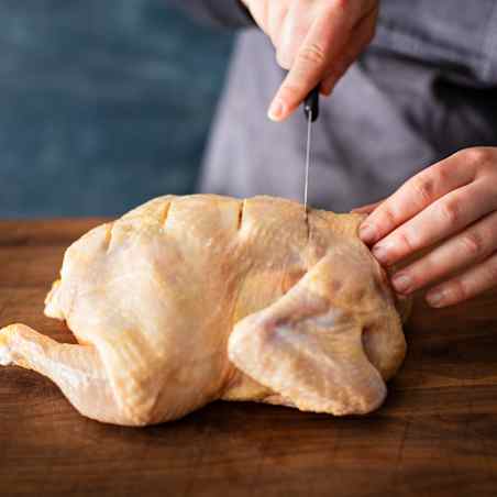 A boning knife is used to score the skin of a whole chicken.