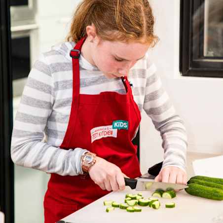 Young child cuts small green vegetables on a cutting board.