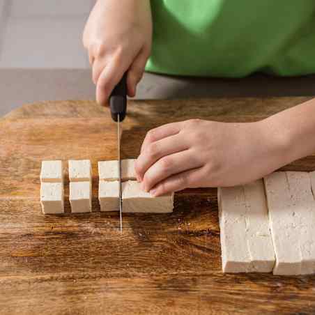 Kitchen knife used to cut small cubes of tofu. Hands hold the knife and tofu.