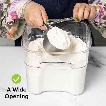 A person dips a measuring cup into a wide container of flour and levels it with a knife. 