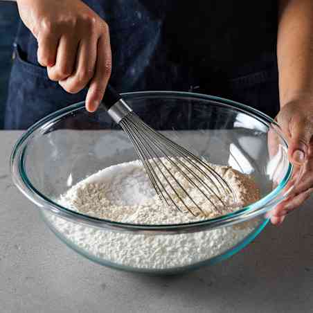 Person whisking dry ingredients in large glass bowl. 